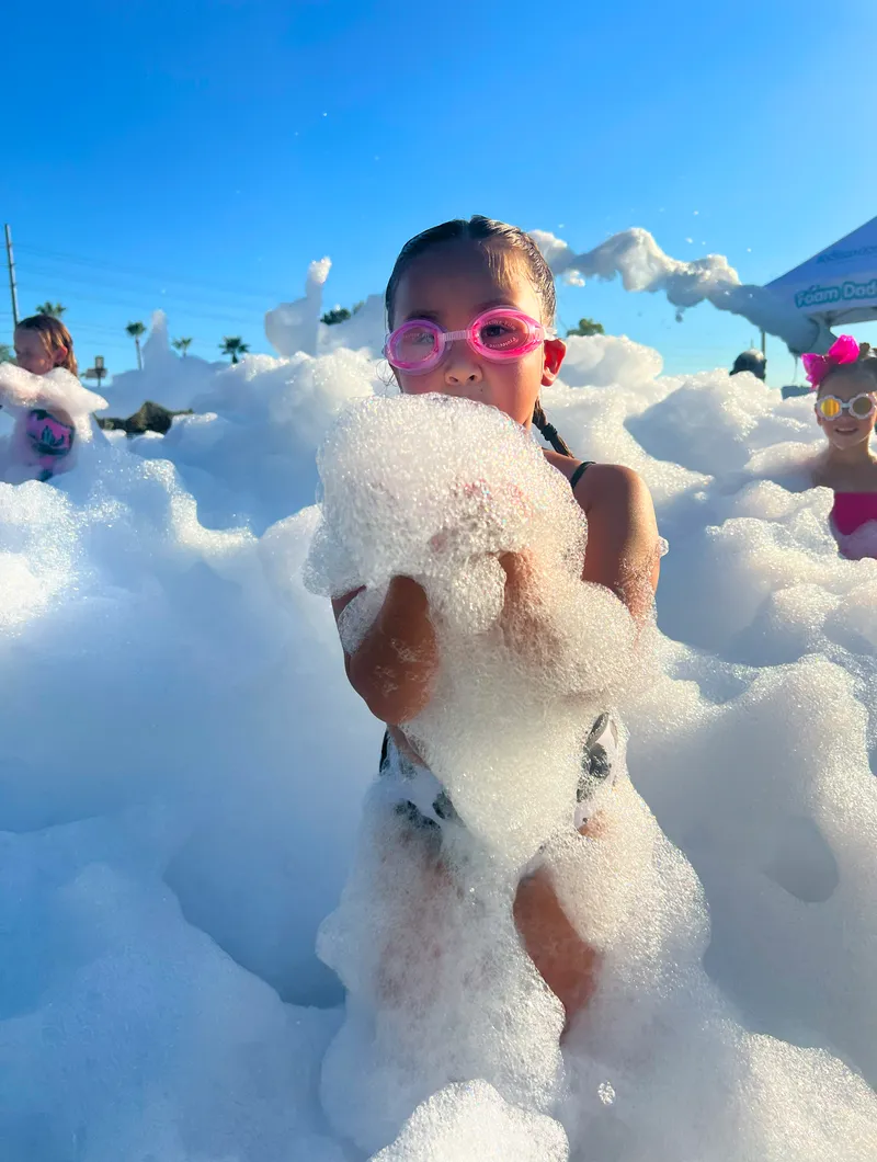 Young child wearing goggles playing in a pile of safe, non-toxic foam at a foam party